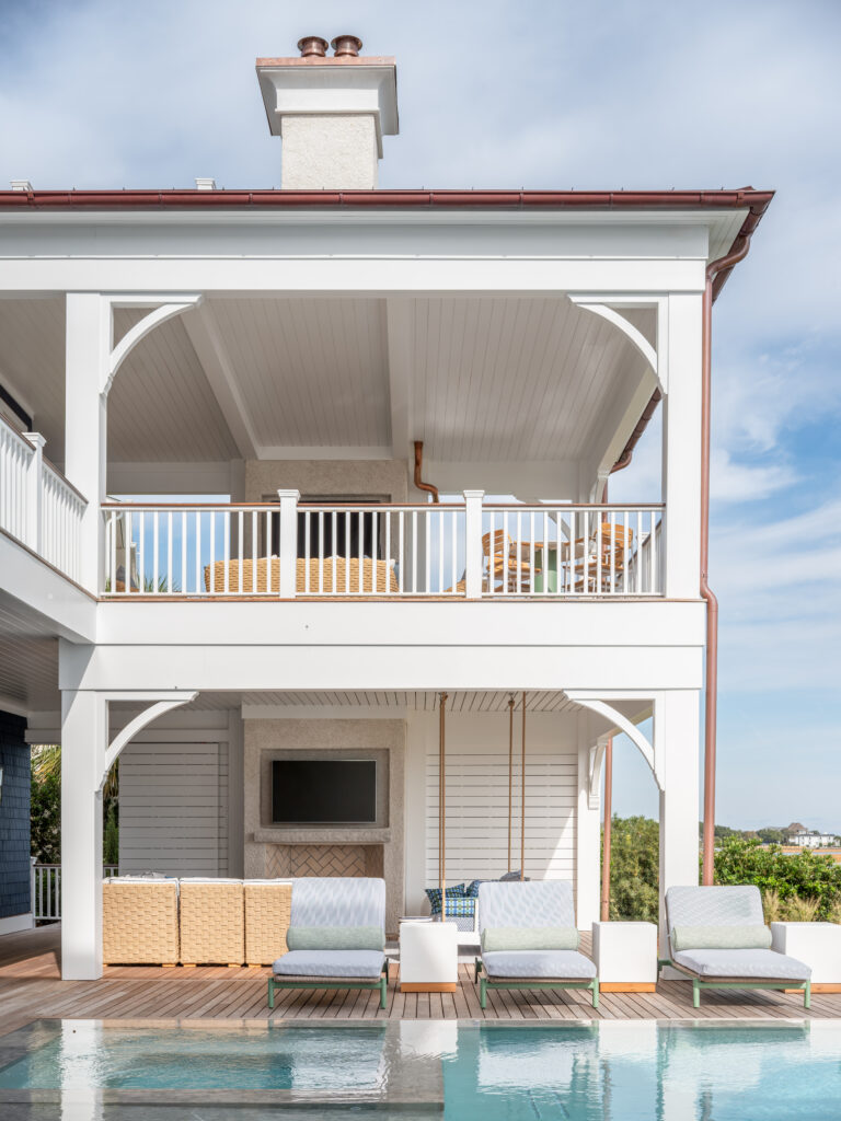 The outdoor spa area of Project Inlet View in Wilmington, NC is shown, where a pool, outdoor living room, fireplace, and TV are showcased.