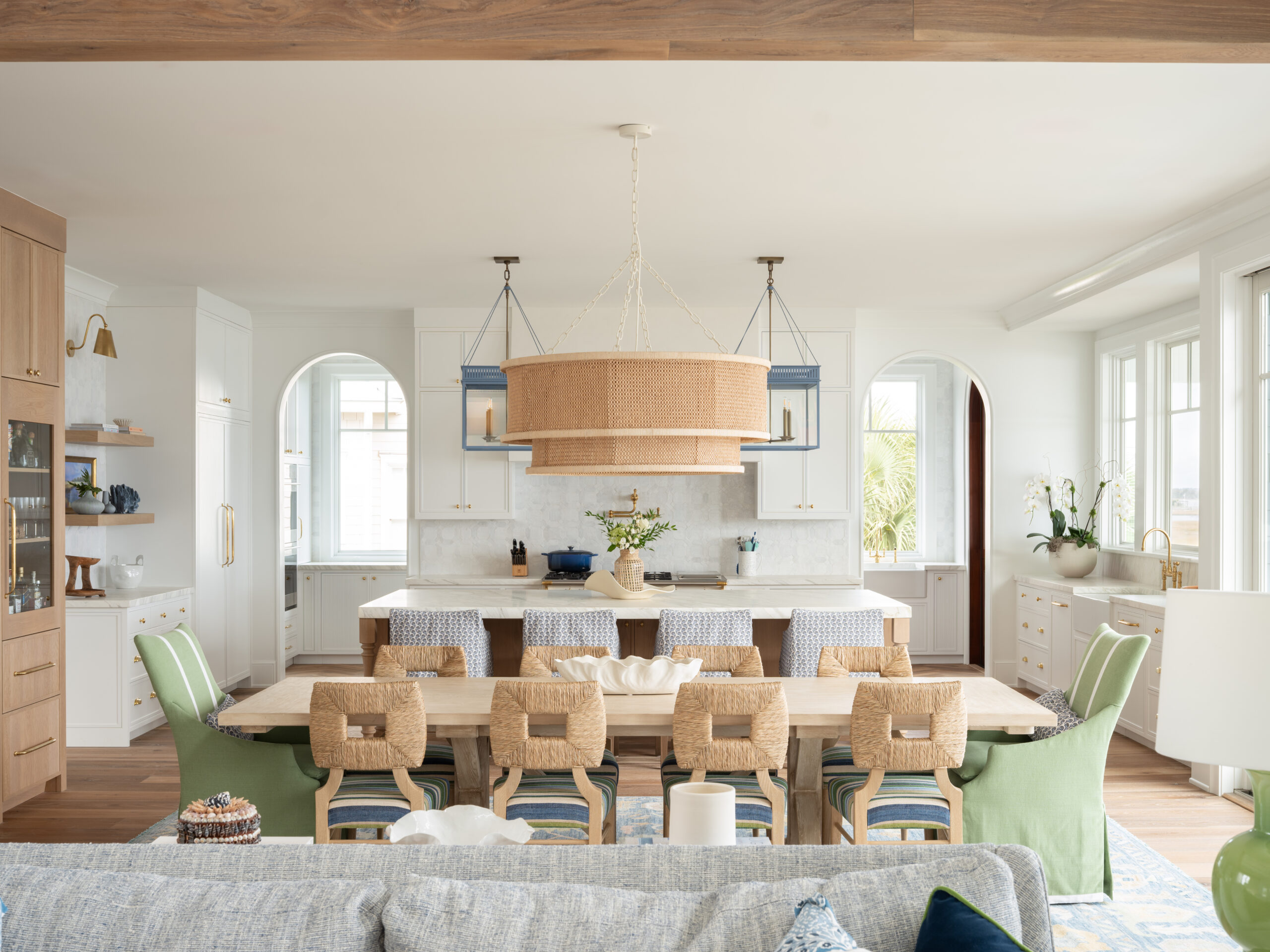 Bright open-concept coastal kitchen at Project Inlet View featuring a custom island, tailored cabinetry, vaulted ceilings with exposed beams, arched openings, abundant natural light, and seamless views toward the Intracoastal Waterway.