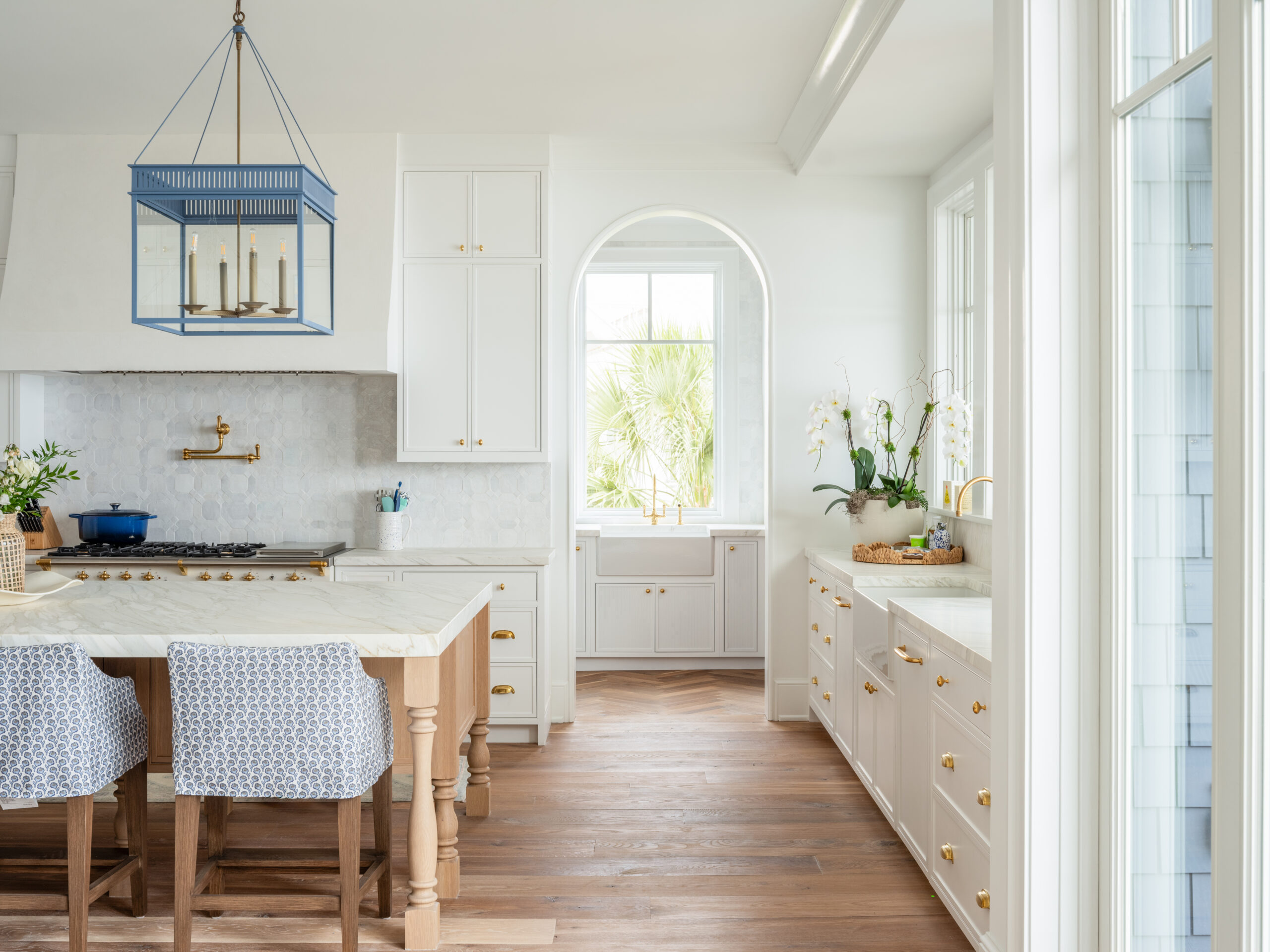 Bright open-concept coastal kitchen at Project Inlet View featuring a custom island, tailored cabinetry, vaulted ceilings with exposed beams, arched openings, abundant natural light, and seamless views toward the Intracoastal Waterway.